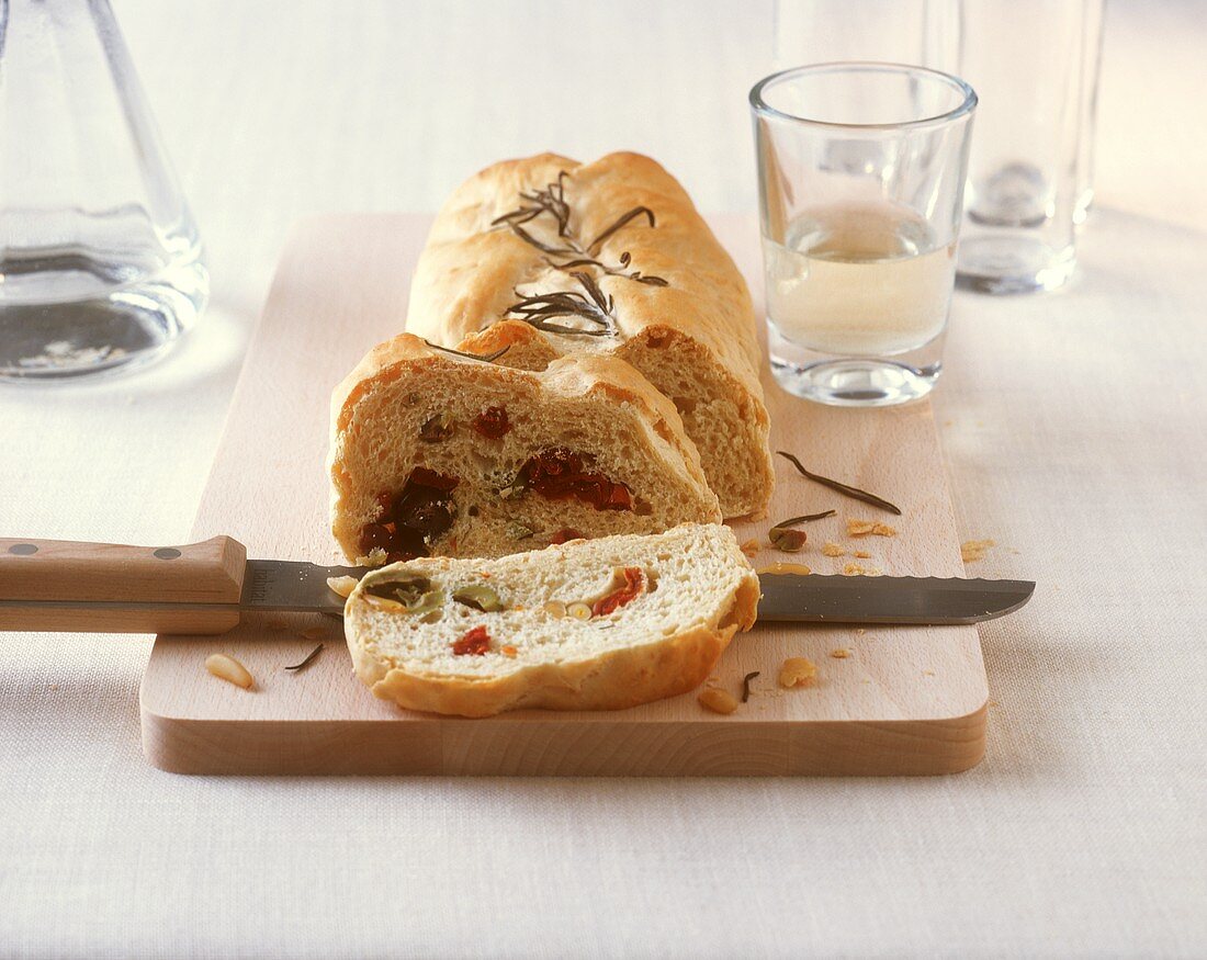 Tomato and olive bread on a wooden board with knife