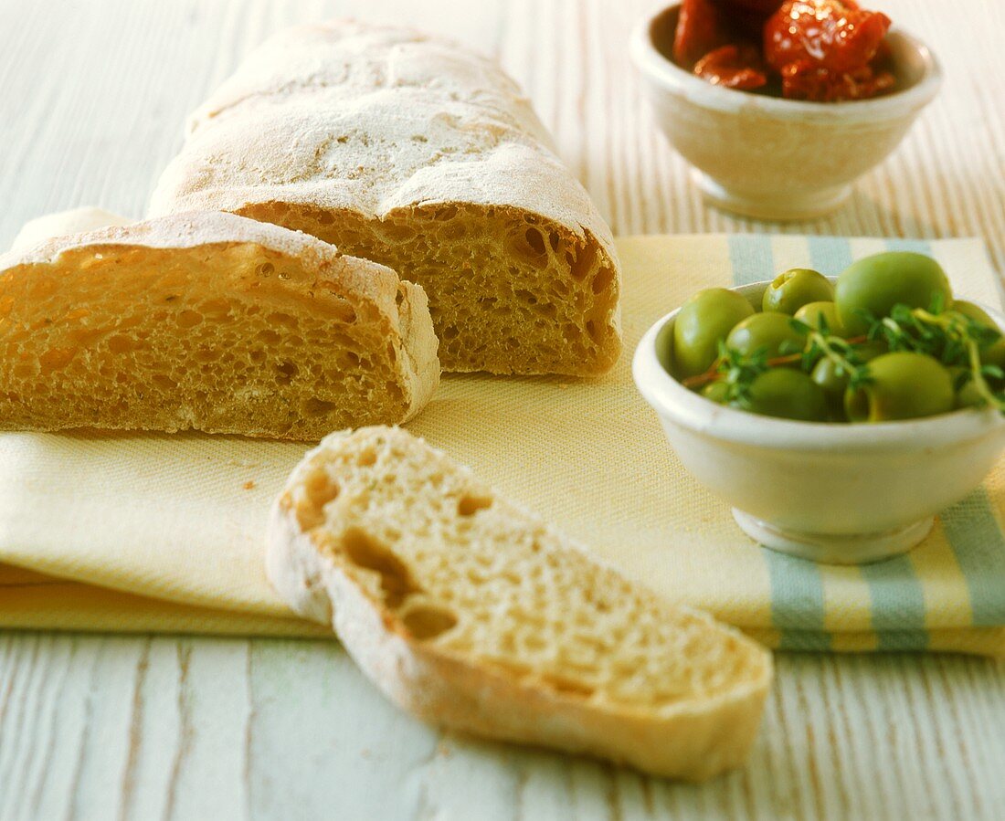 Ciabatta with bowl of green olives on kitchen cloth