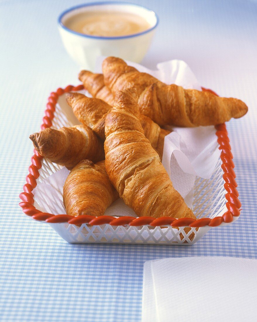 Croissants in bread basket, bowl of white coffee behind