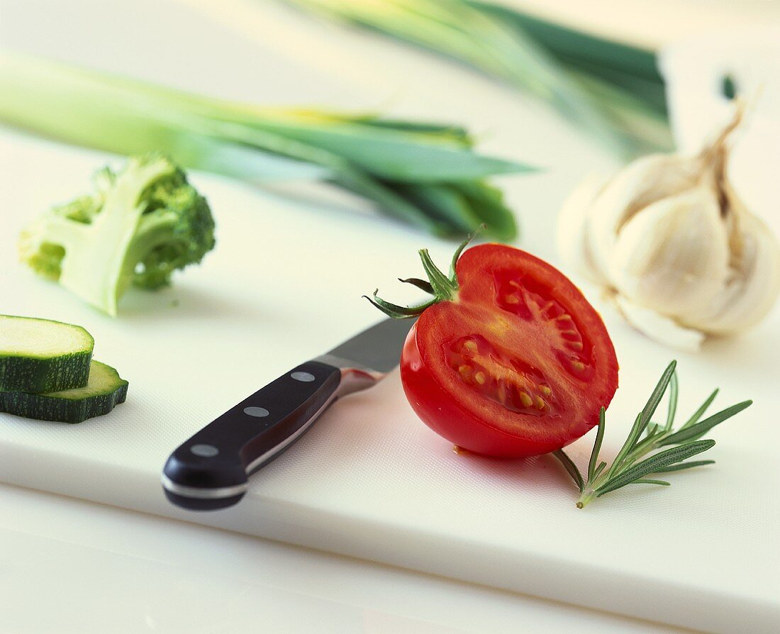 Half a tomato, rosemary and vegetables with knife