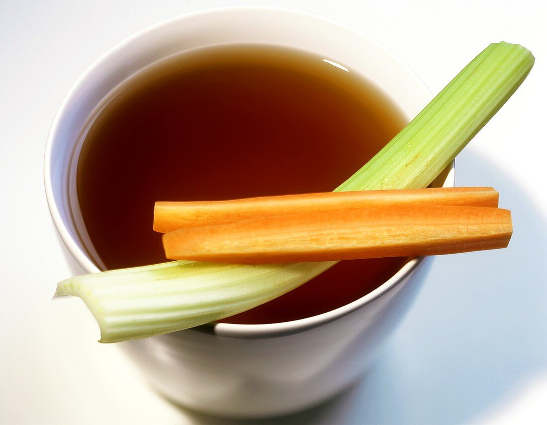 Vegetable stock in a bowl with stick of celery and carrot