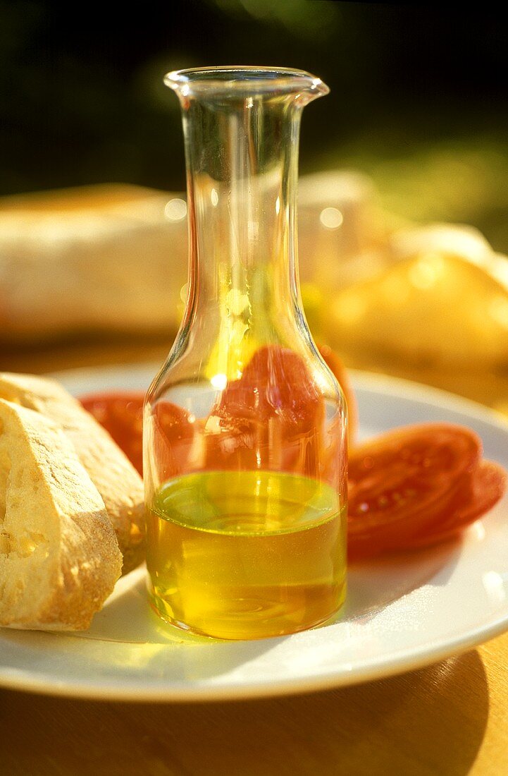Kleine Glasflasche mit Olivenöl, mit Tomaten und Brot daneben