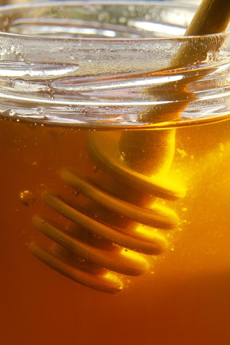 Honiglöffel in einem Glas mit flüssigem Honig (Nahaufnahme)