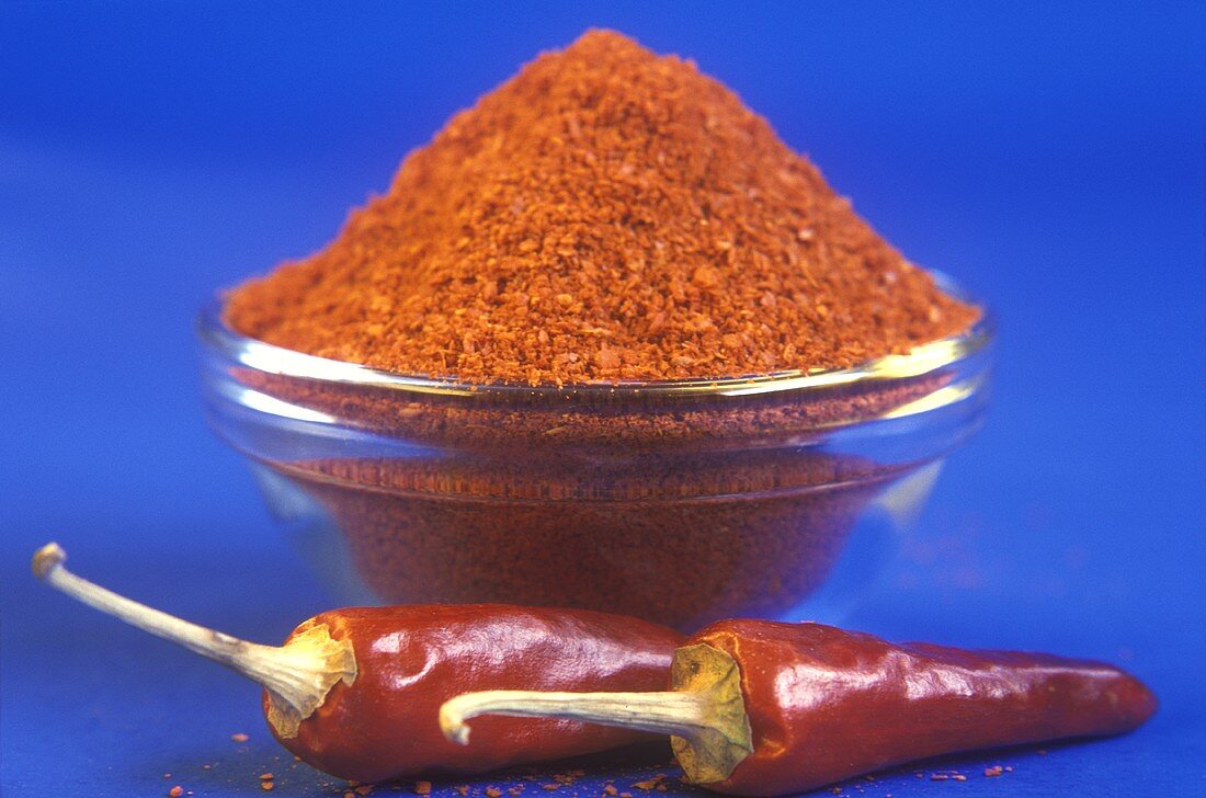 Zwei rote Chilischoten und ein Schälchen mit Chilipulver