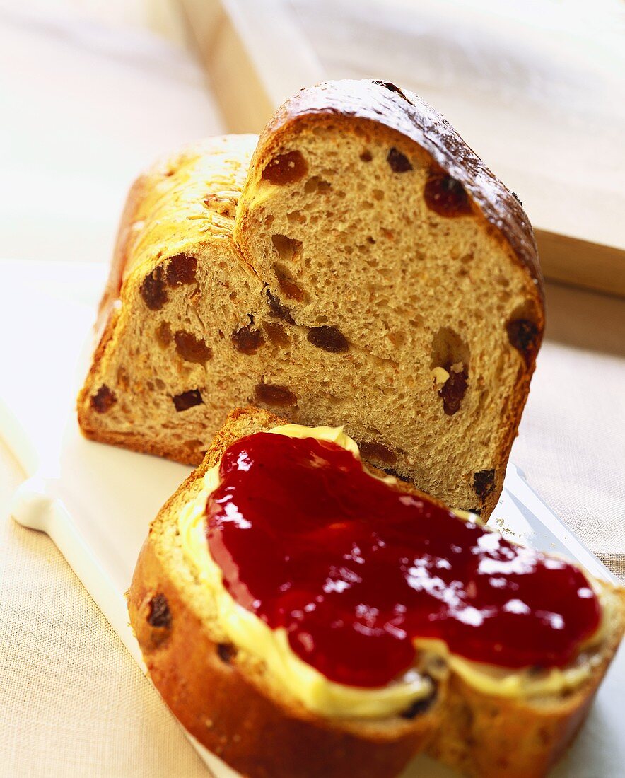 Piece of raisin bread and slice with butter and jam