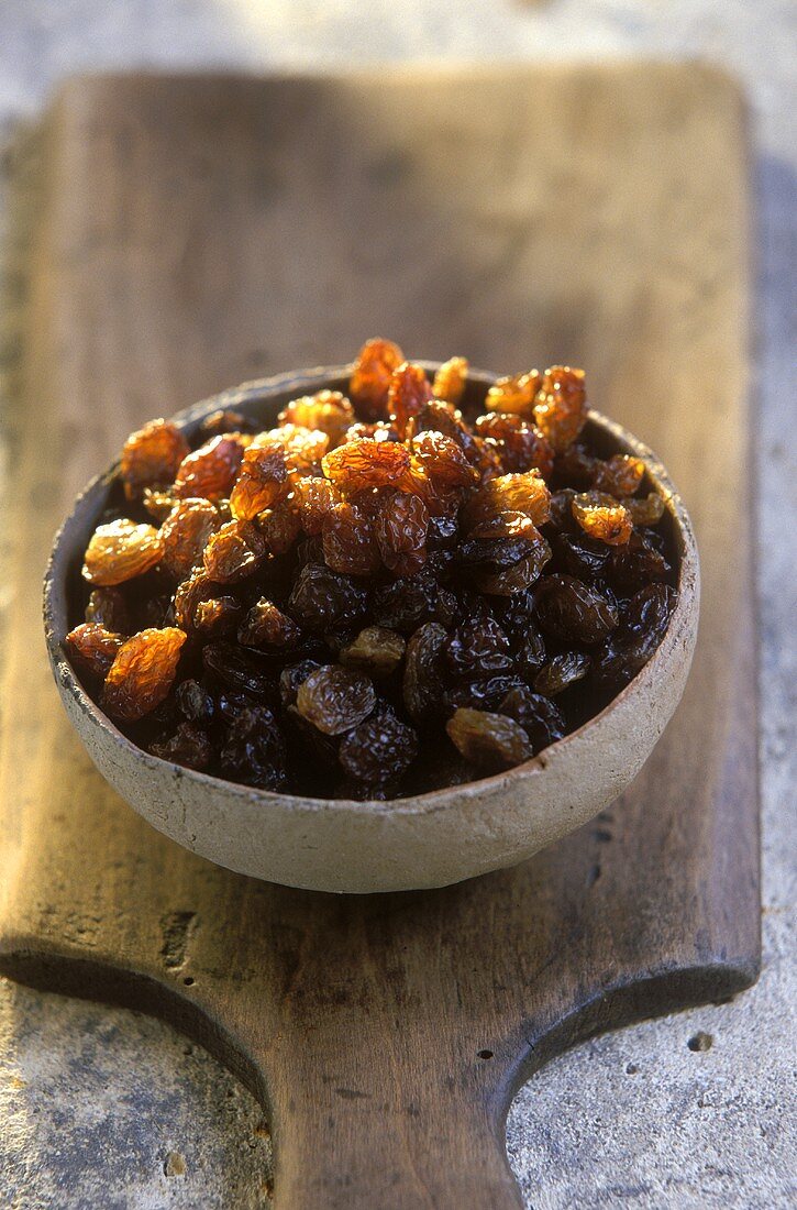 Terracotta bowl of raisins on a wooden board