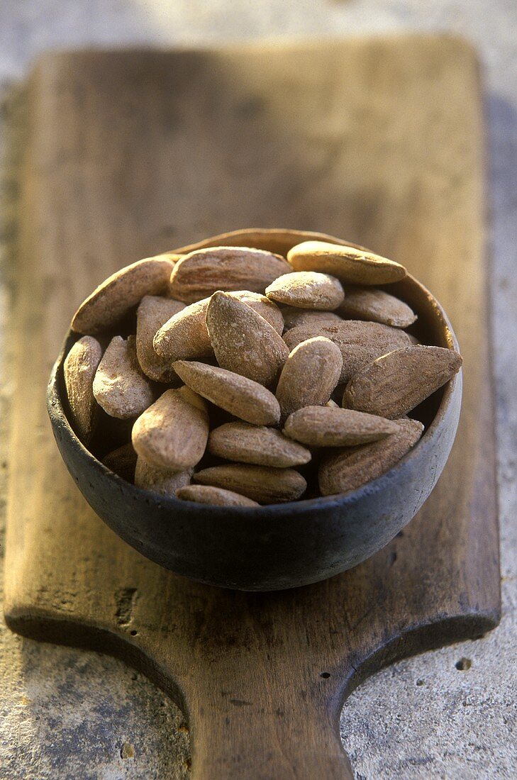 Terracotta bowl of salted almonds on a wooden board