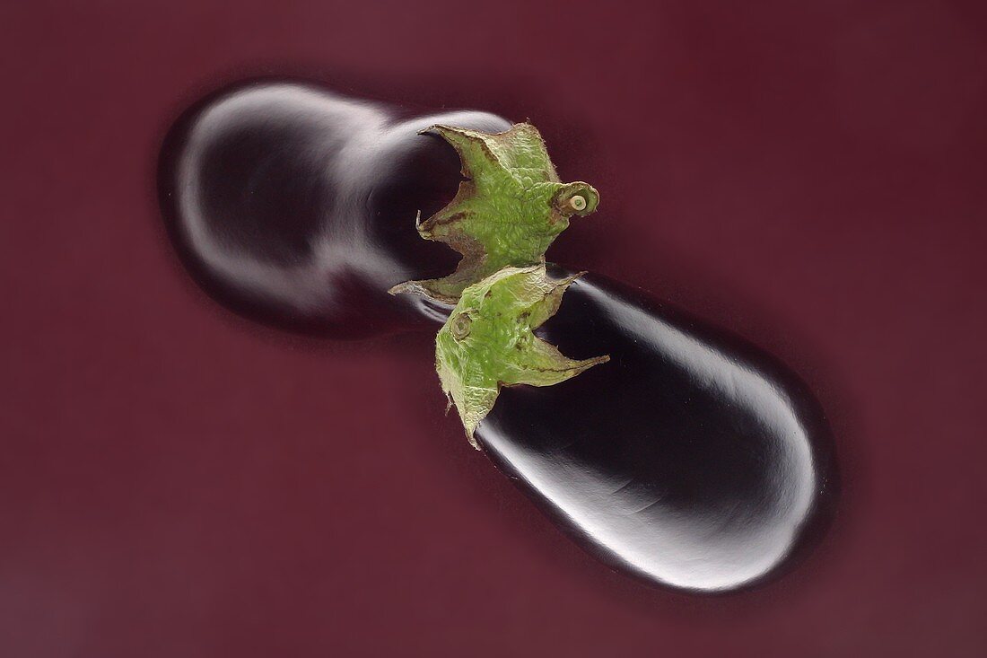 Two aubergines against brown background