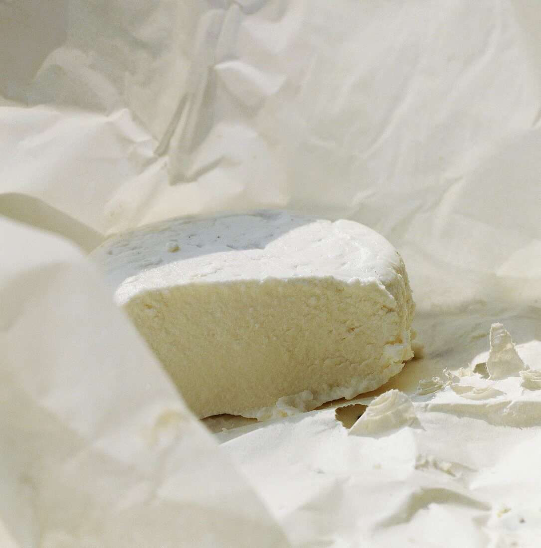 Fresh goat's cheese in greaseproof paper, a piece cut off