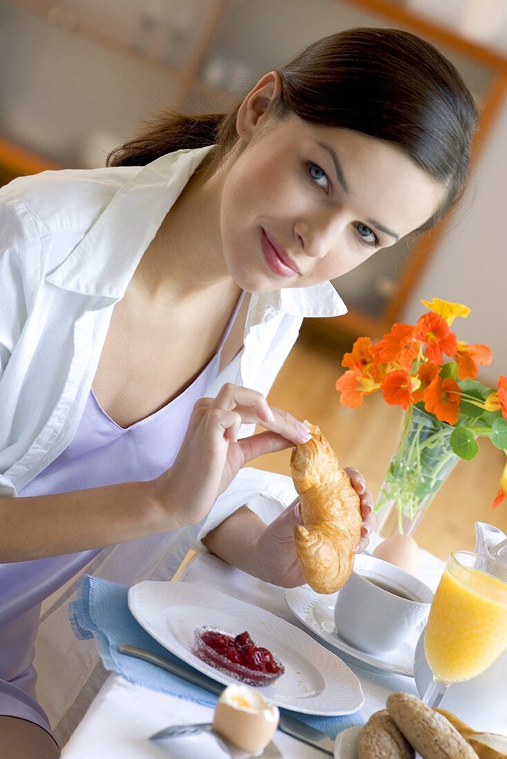 Junge Frau isst Croissant am Frühstückstisch