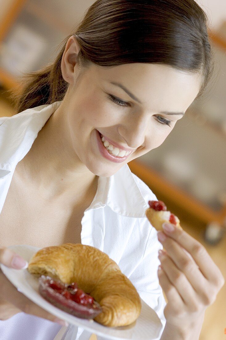 Young woman holding plate with croissant and jam