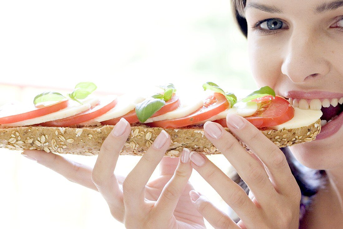 Junge Frau isst Tomaten-Mozzarella-Sandwich