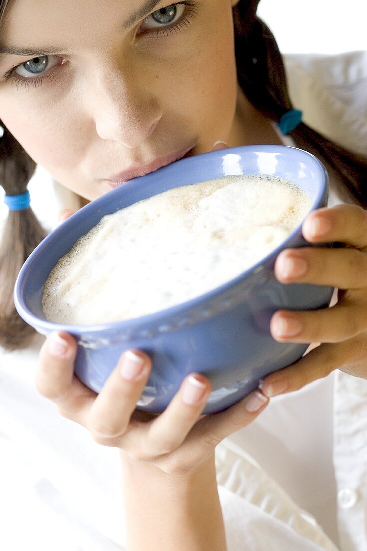 Young woman drinking white coffee from bowl (close-up)