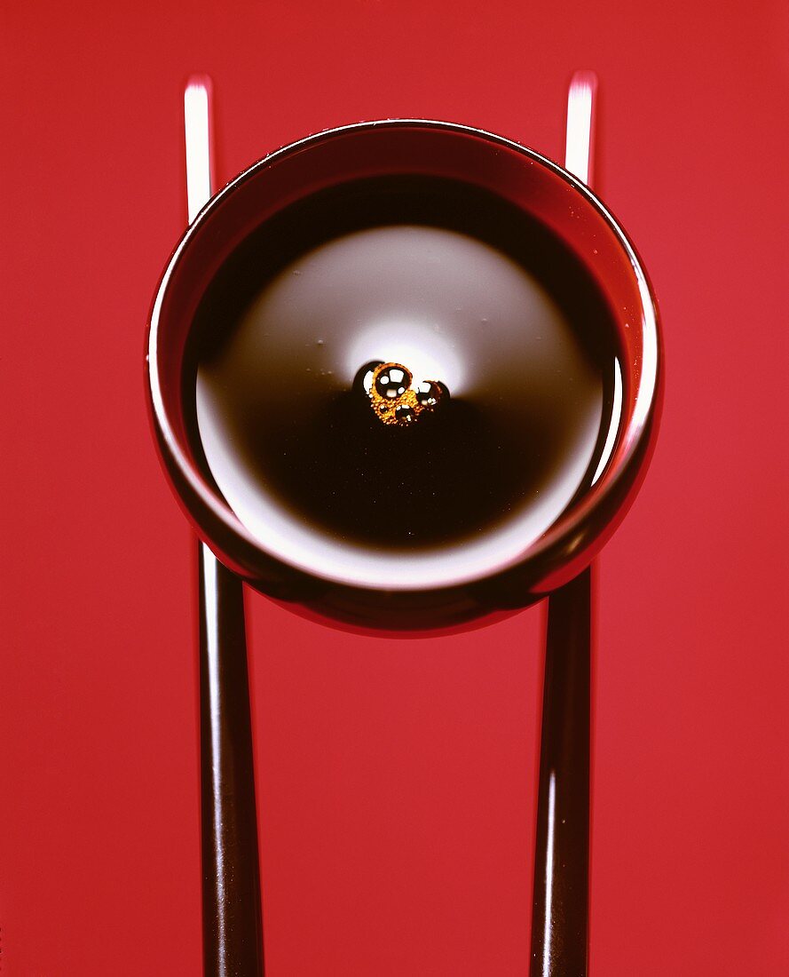 Bowl of soy sauce against red background