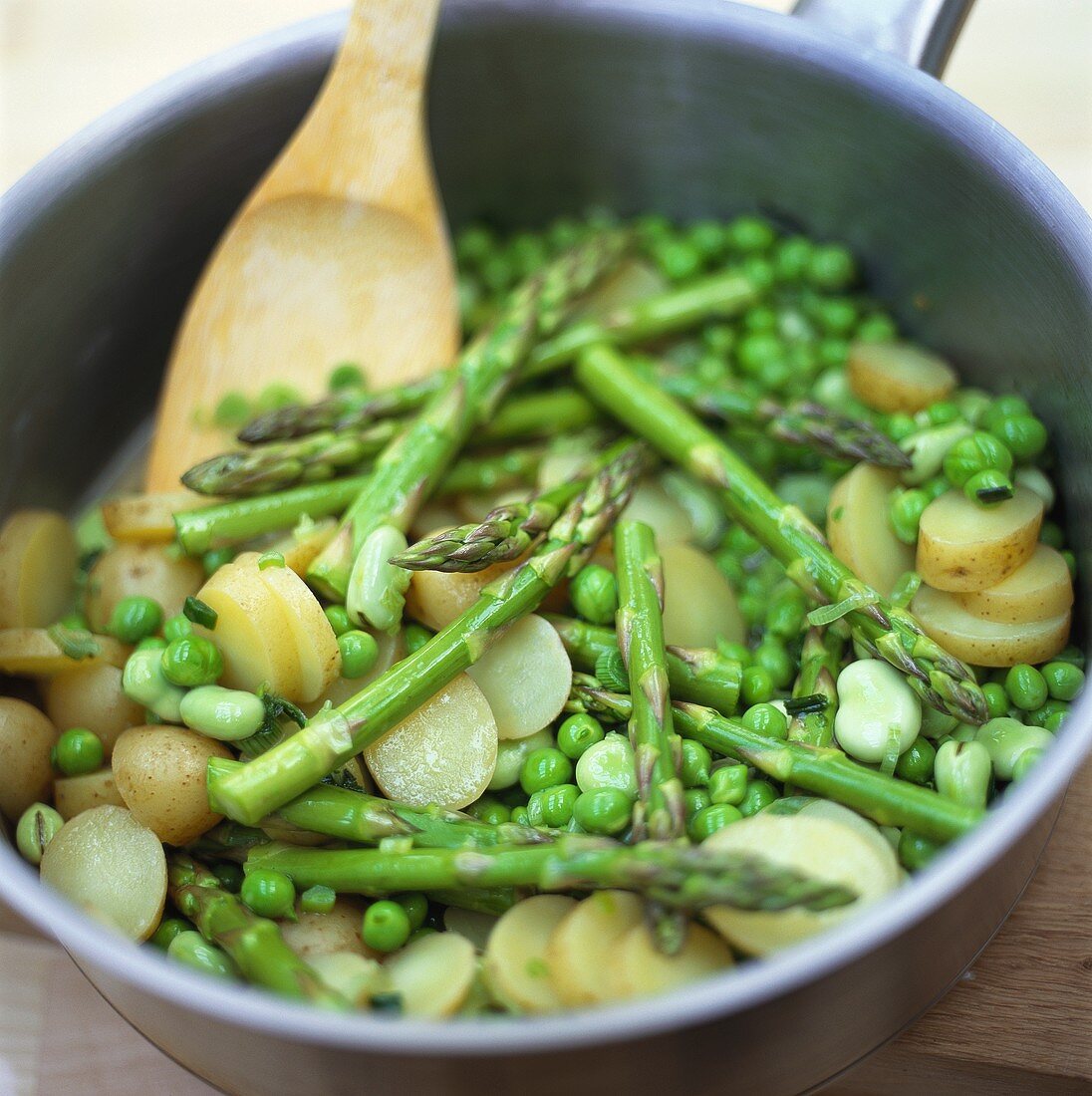 Green asparagus with potatoes and peas in frying pan