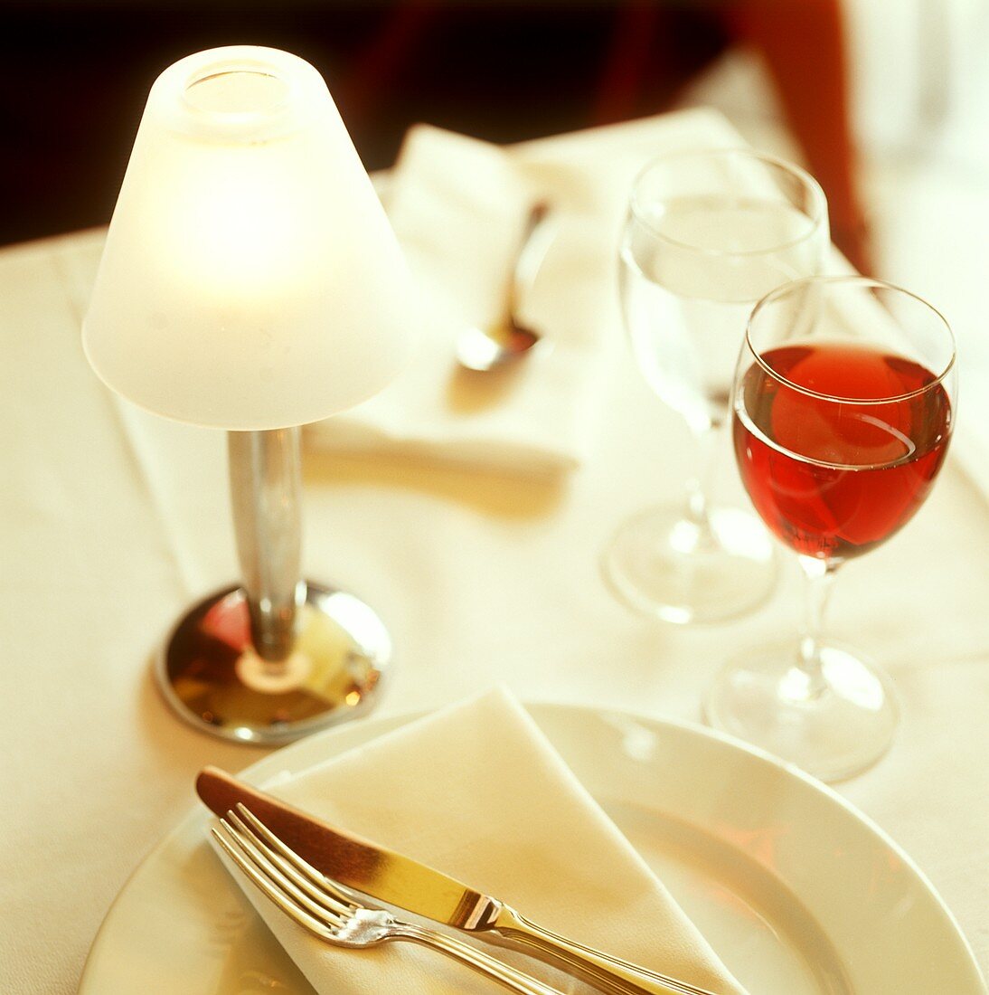 Place-setting with red wine and mineral water and a table lamp