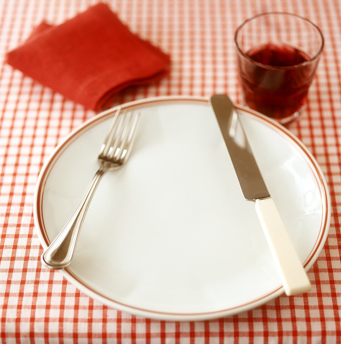Gedeck mit Rotwein für eine Person auf kariertem Tischtuch