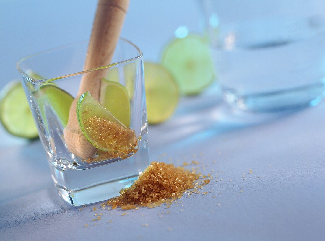 Glas mit Caipirinha-Zutaten (brauner Zucker,Stössel,Limetten)