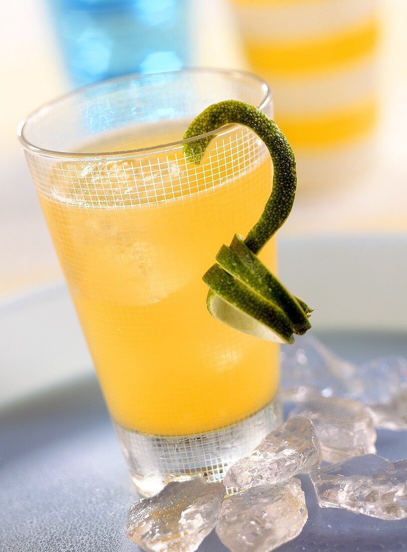 Yellow fruit cocktail in glass garnished with lime peel