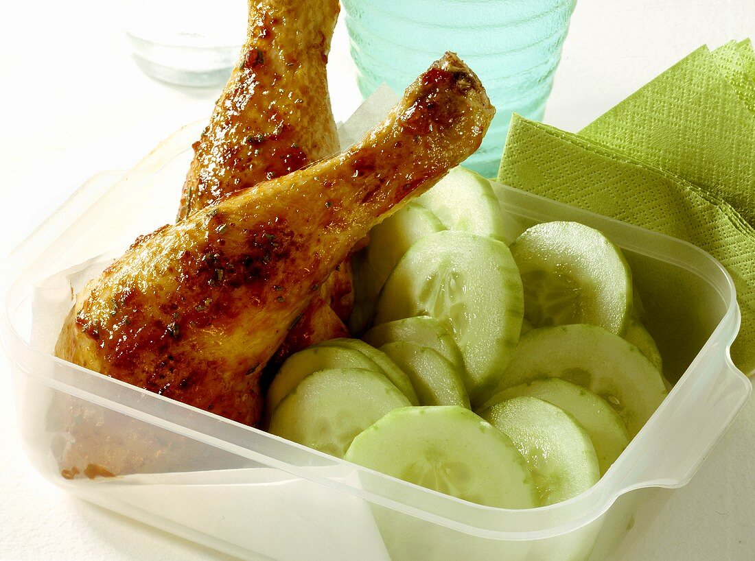 Spicy chicken legs with cucumber slices in plastic container