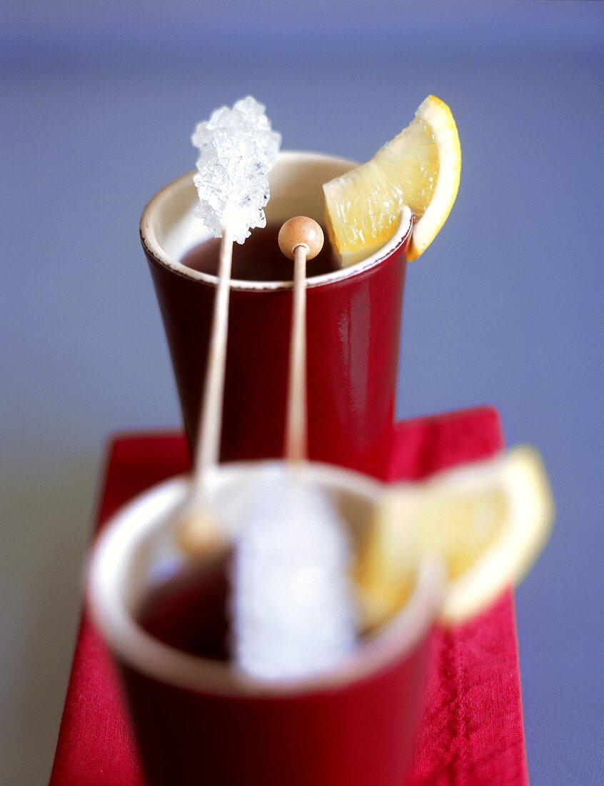 Two beakers of fruit tea with lemon wedges, sugar sticks