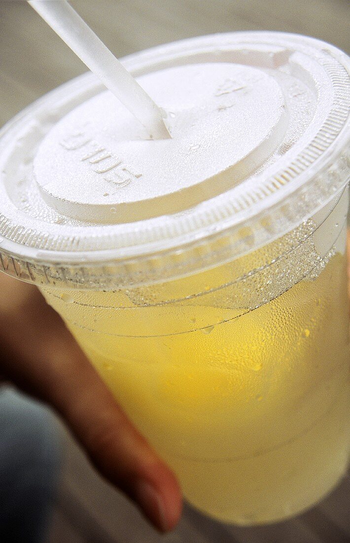 Hand holding plastic take-away container of fresh lemonade
