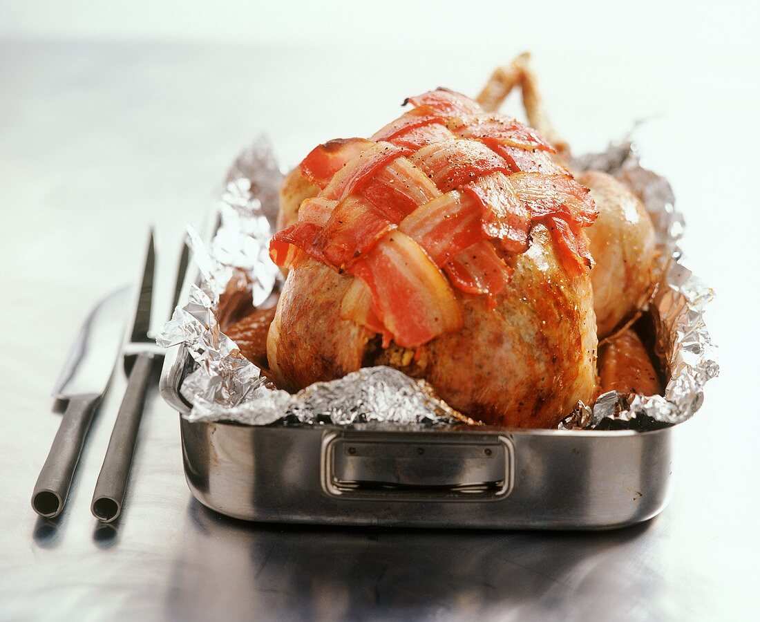 Whole roast chicken with bacon in roasting dish