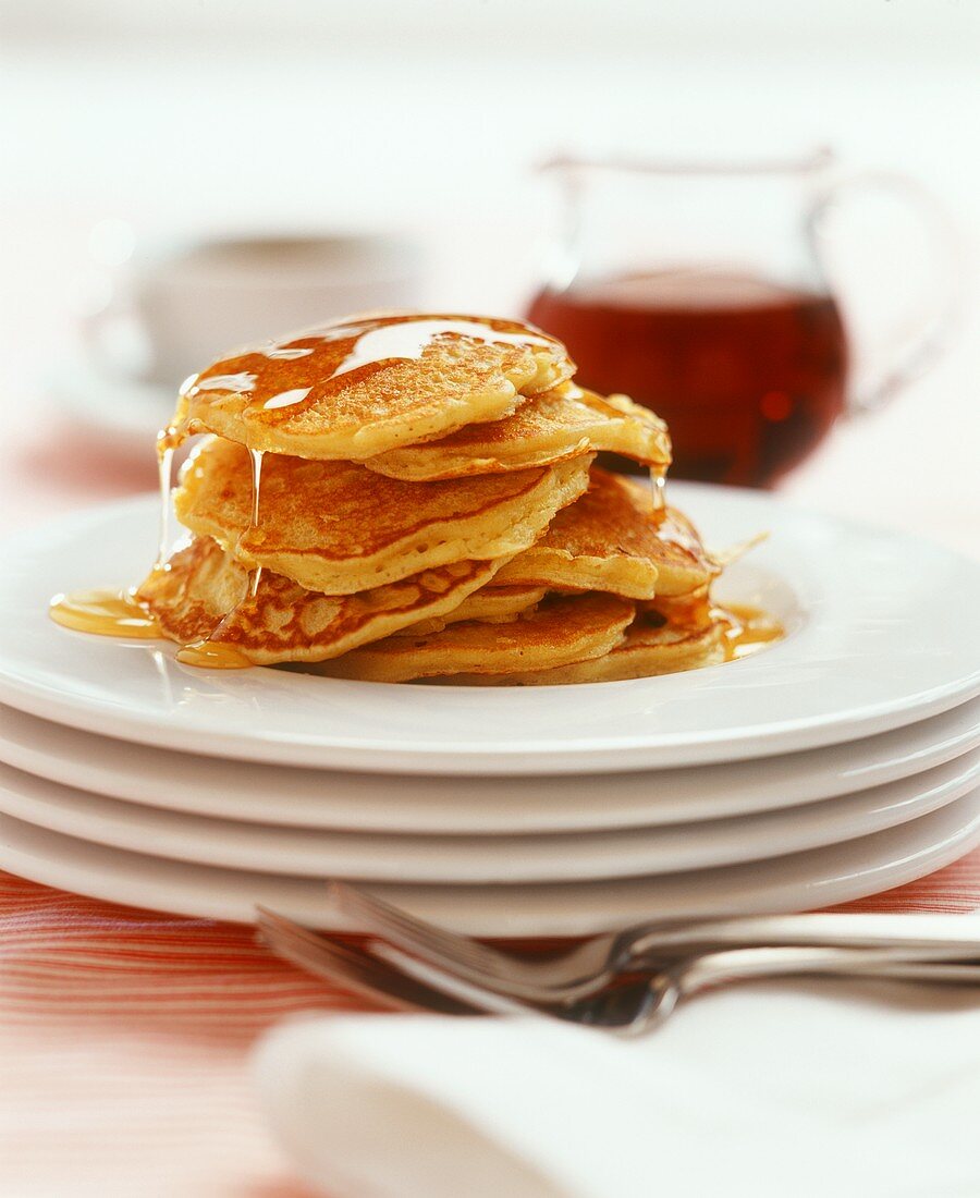 Eight pancakes with maple syrup on a pile of plates