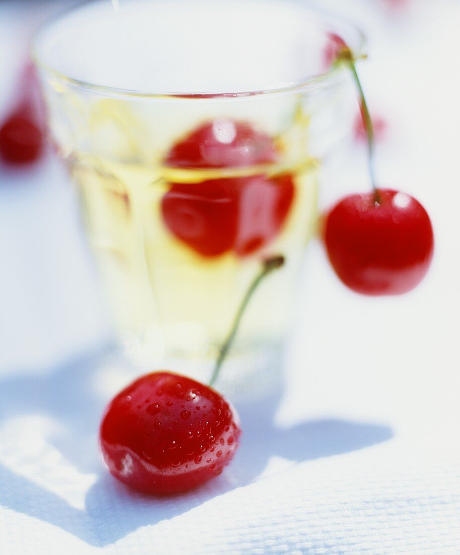 Kirsche mit Wassertropfen, dahinter Kirschenpaar und Glas