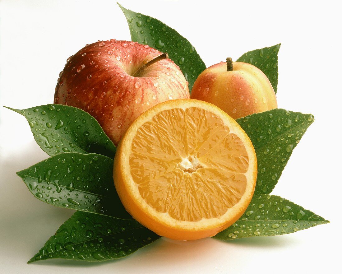 Halbe Orange, Apfel und Nektarine zwischen Orangenblättern