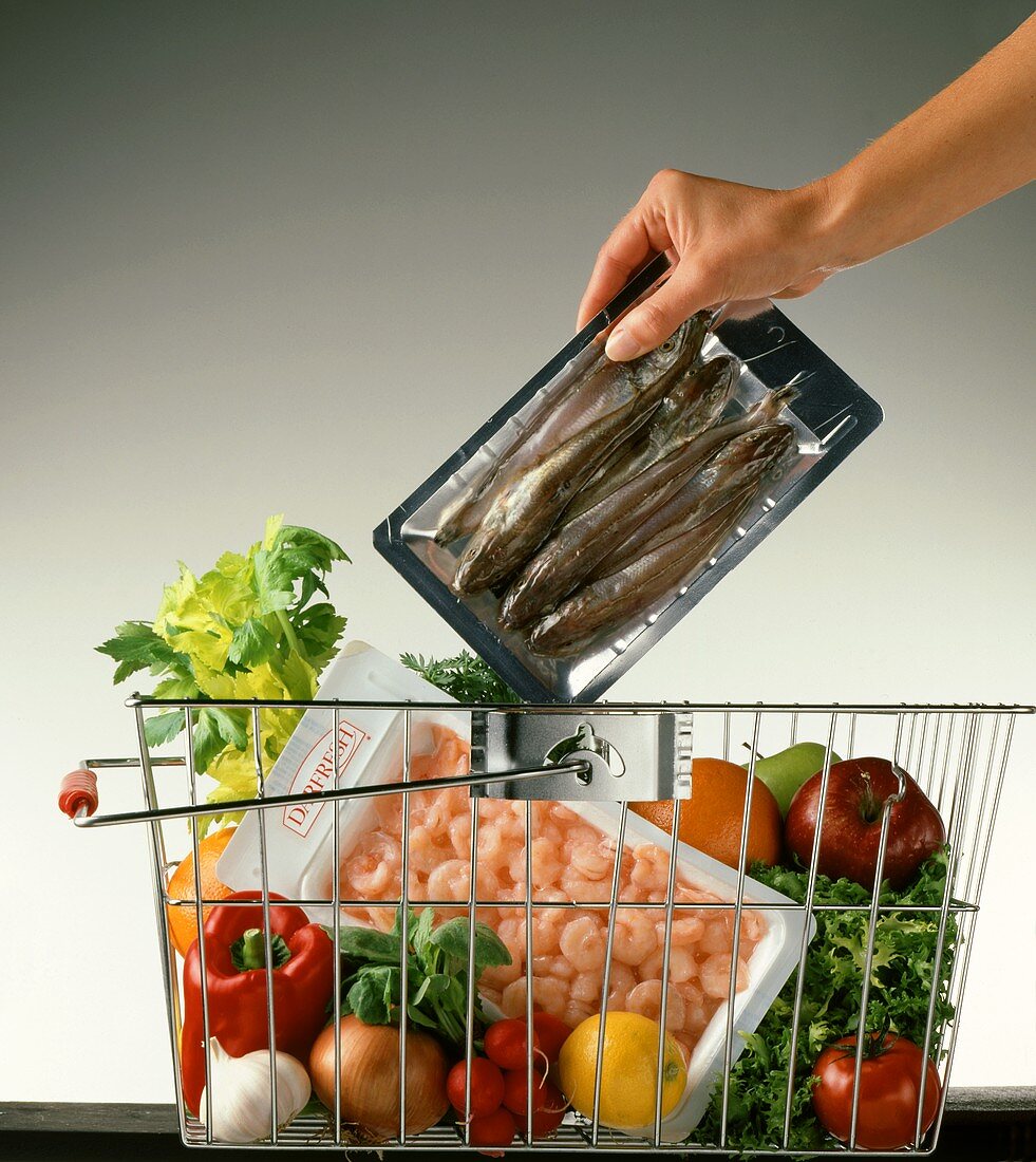 Hand placing packed fish into shopping basket of shopping
