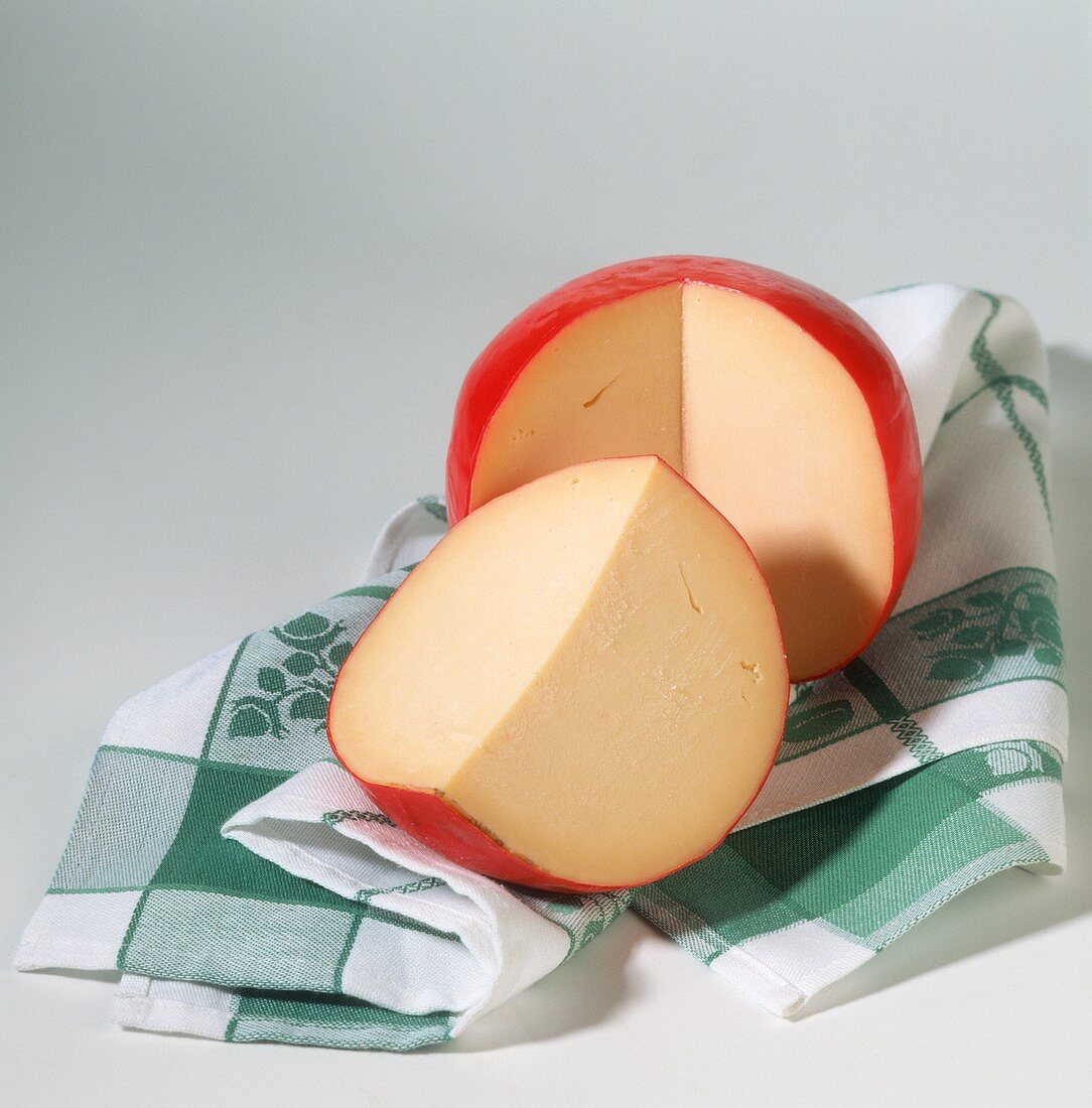 Whole Edam cheese, with piece cut off, on kitchen cloth