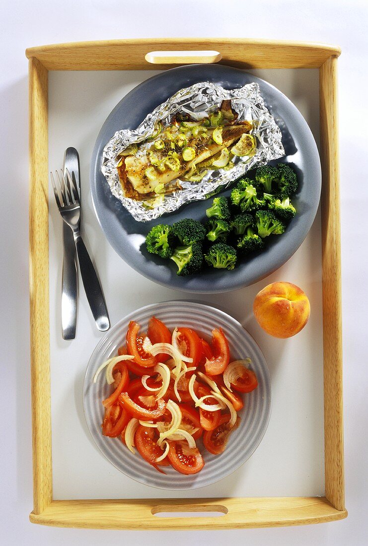 Sole cooked in foil, broccoli and tomato salad on tray