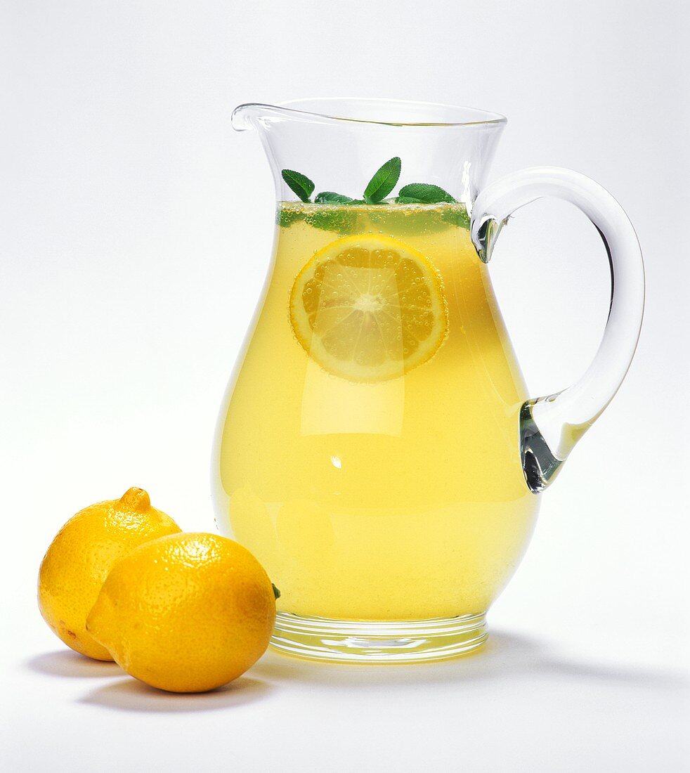Glaskrug mit Zitronenlimonade, daneben Zitronen