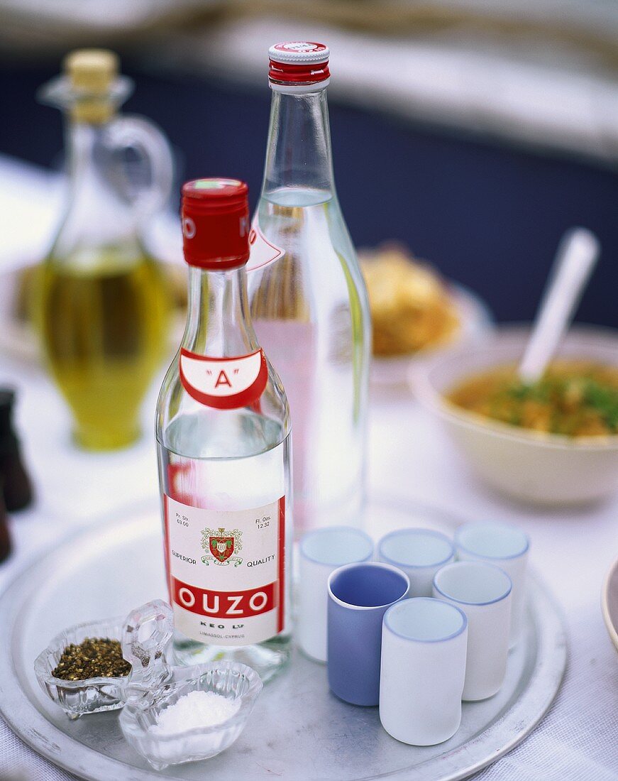 Two bottles of Ouzo on tray with glasses, salt and pepper
