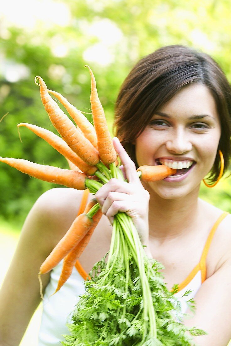 Woman with a bunch of carrots biting into one of them