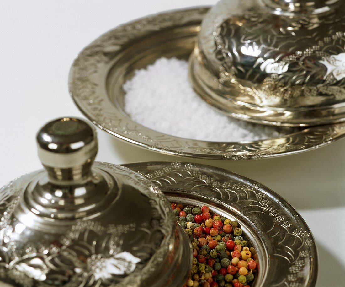 Coloured peppercorns and coarse salt on silver platters