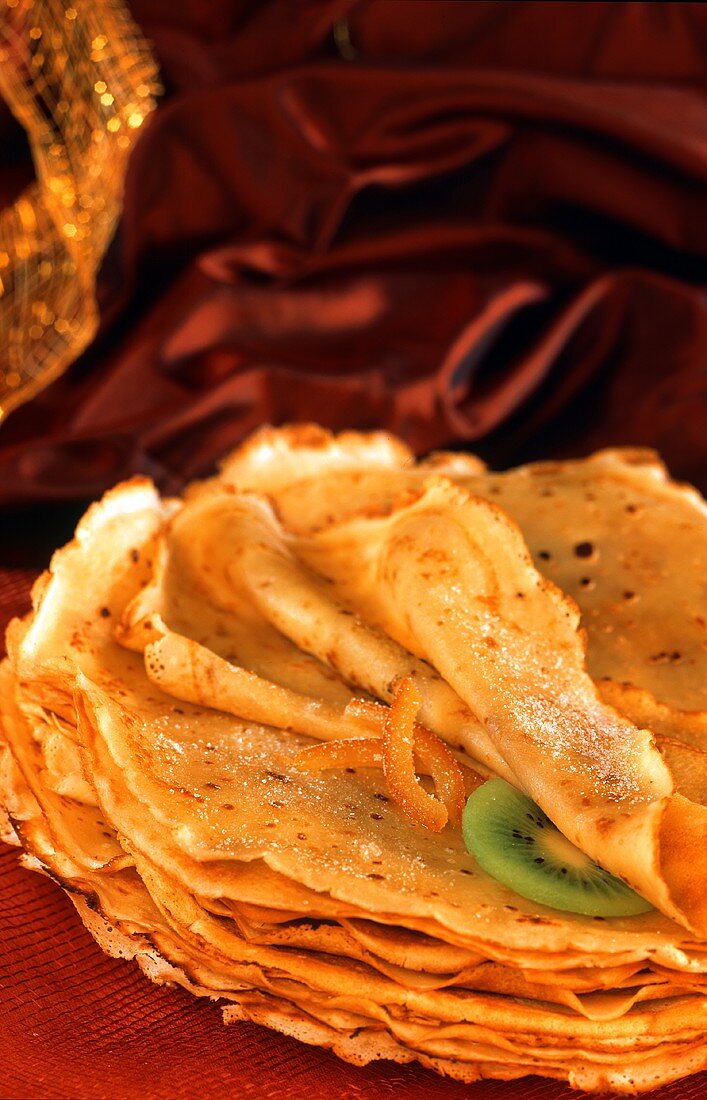 Pile of crepes with icing sugar, slice of kiwi, orange peel