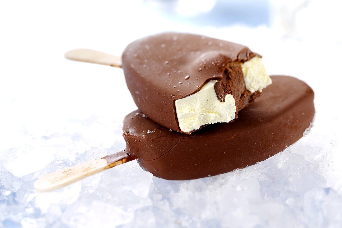 Two vanilla and chocolate ices on sticks, one with a bite taken