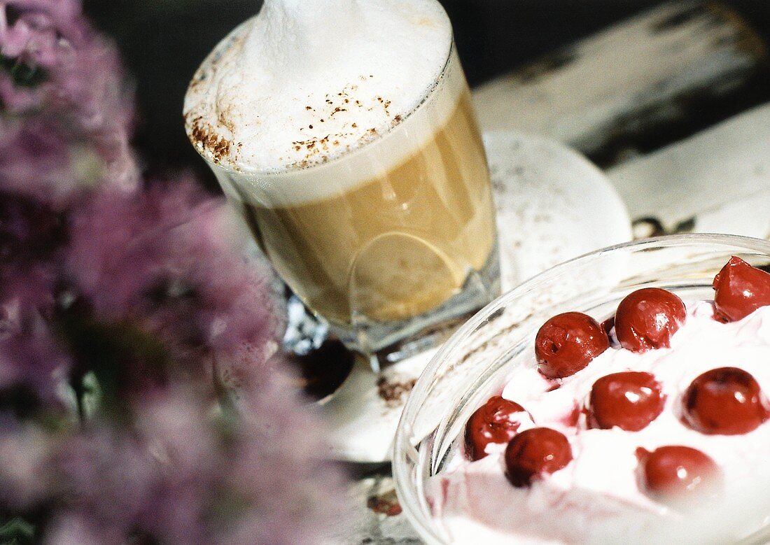 Glass of latte macchiato and quark dessert with cherries