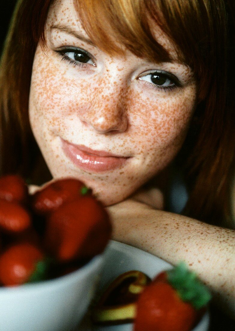 Freckled woman in front of a bowl of strawberries