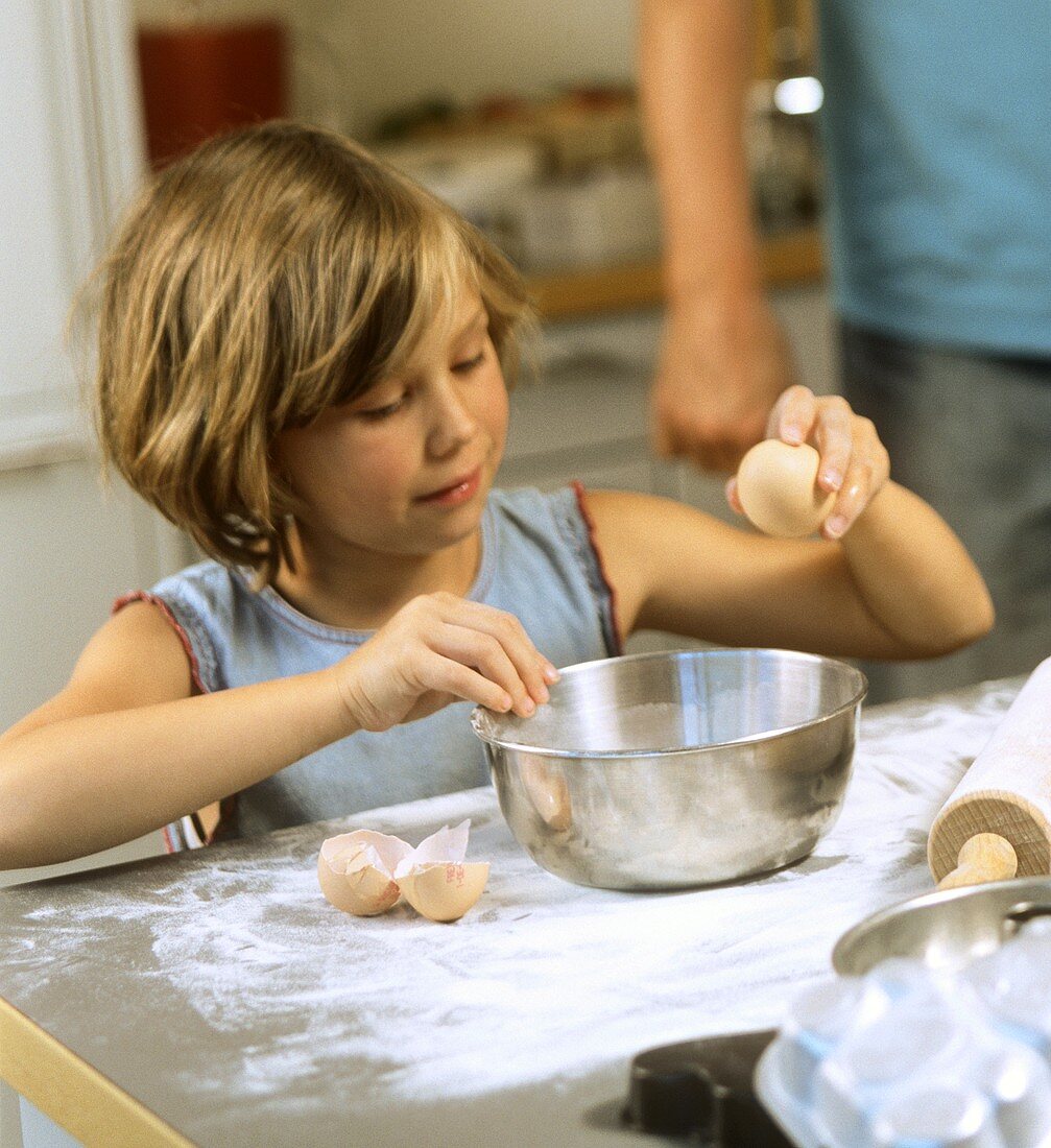 Baking scene: a little girl cracking an egg