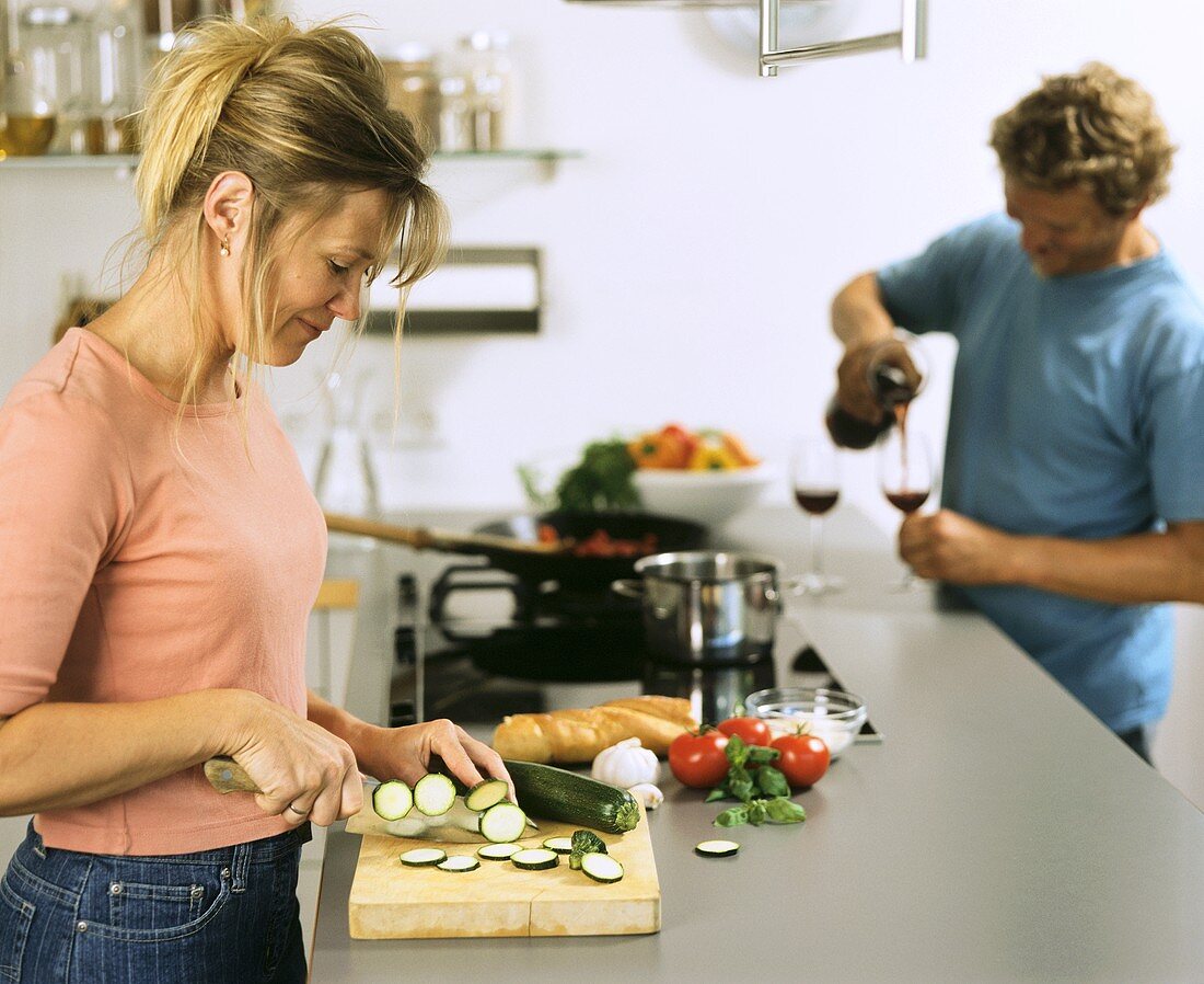 Kitchen scene: woman cutting courgette, man pouring wine