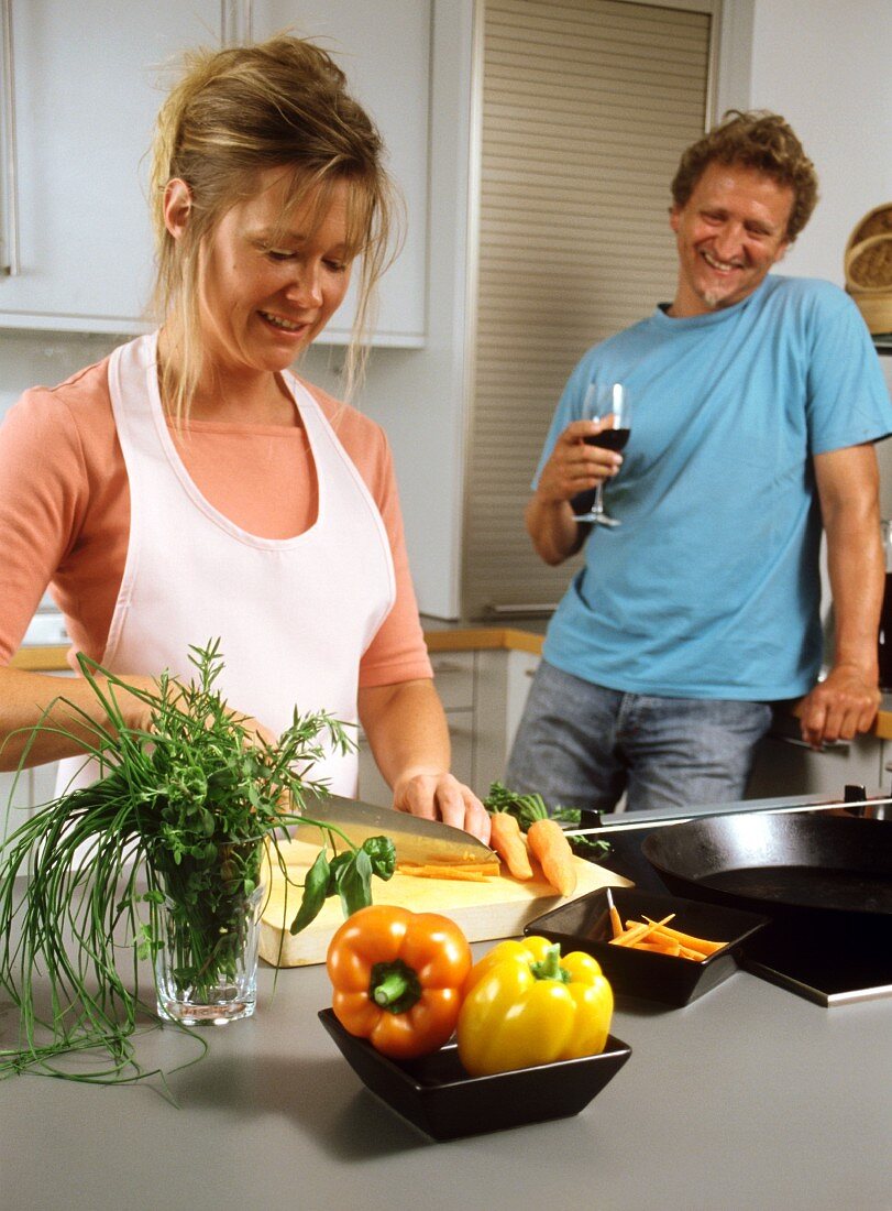 Küchenszene: Frau schneidet Gemüse, Mann mit Weinglas