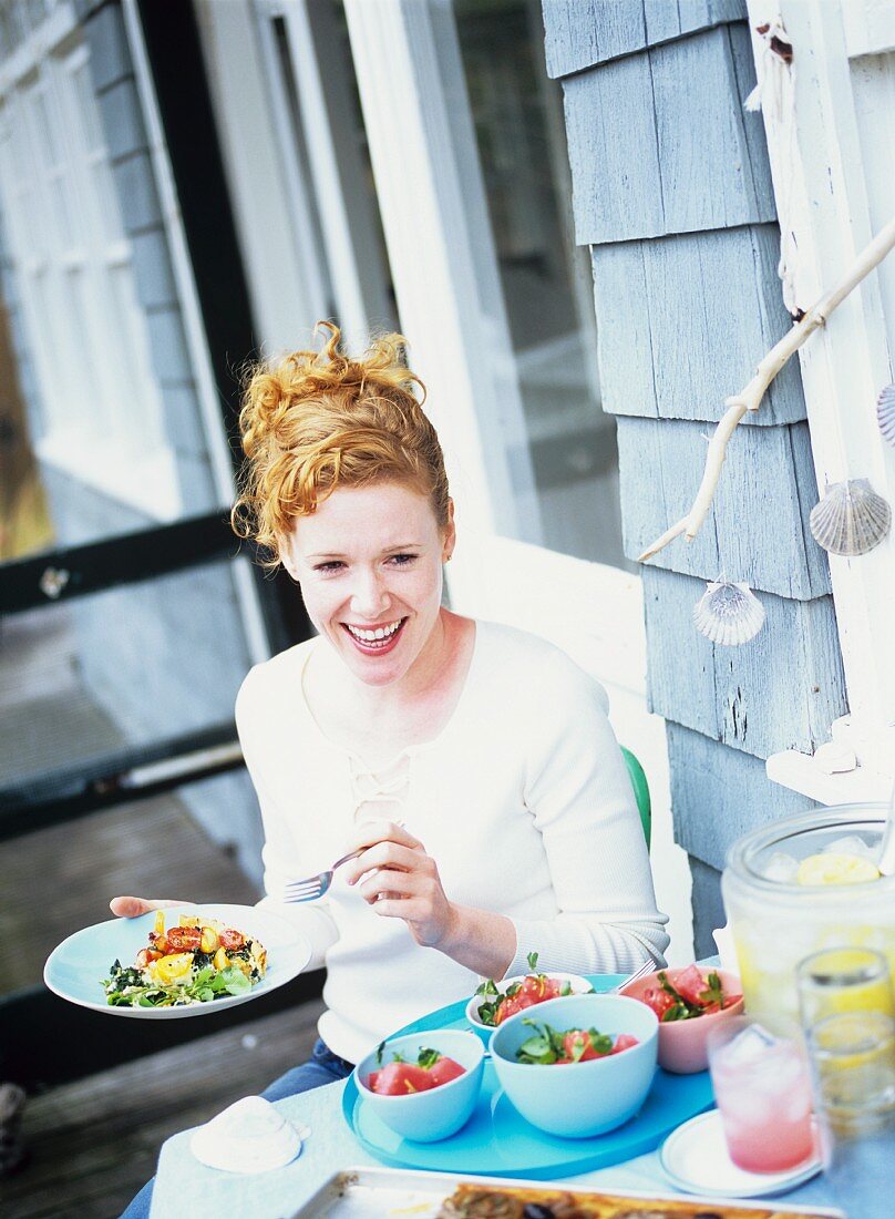Woman at terrace table with tomato quiche, melon salad on side