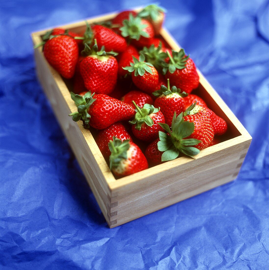 Erdbeeren in einem Holzkistchen auf blauem Untergrund