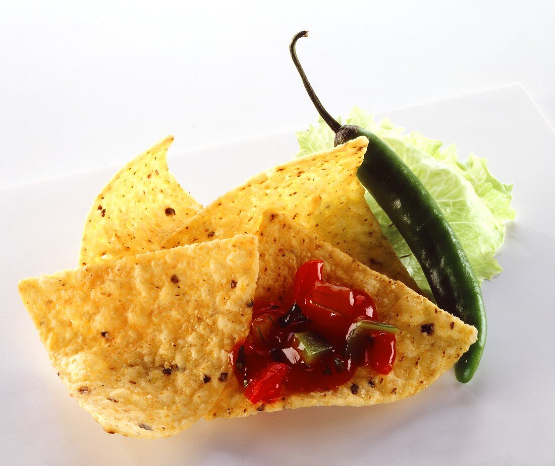 Taco chips with red chili sauce, green chili pepper beside them