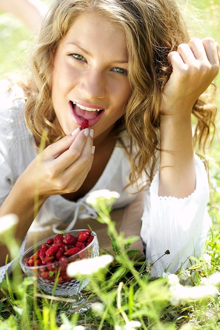 Young woman in grass with a bowl of wild strawberries