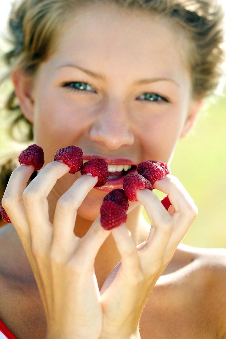 Young woman with raspberries on her finger tips