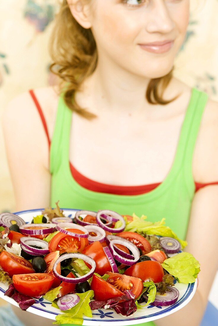 Junge Frau hält Teller Salat mit Tomaten, Oliven, Zwiebeln